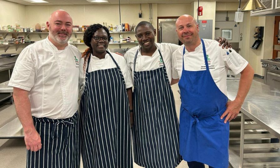 Lynette Nyagaya with chefs in a professional kitchen, smiling