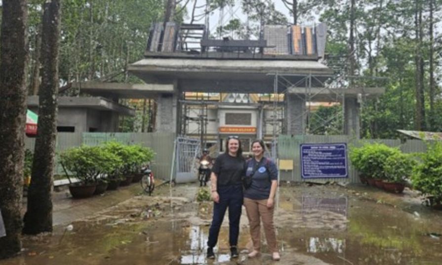 Mikaela stands with her friend in front of a worksite in Vietnam.