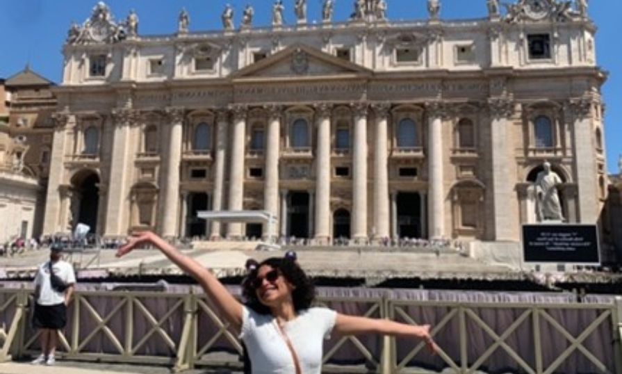 Sara Varga poses joyfully in front of St. Peter's Basilica during her Italy trip on a sunny day.