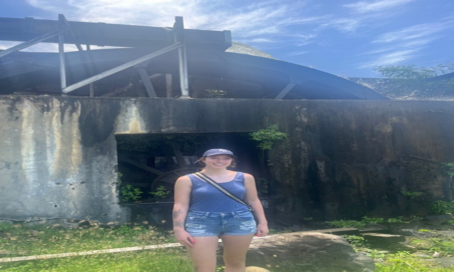 Charlee Orde standing, smiling by a historic mill in Grenada, discovering culture and Caribbean history.