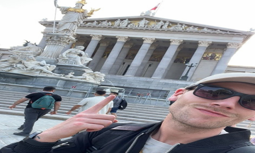 Zachary smiles and points at the Austrian Parliament Building in Vienna