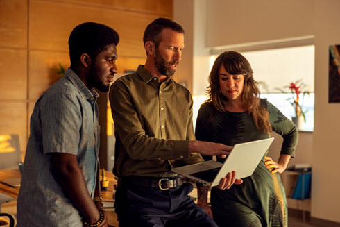 Instructor standing with two students looking at laptop screen. 