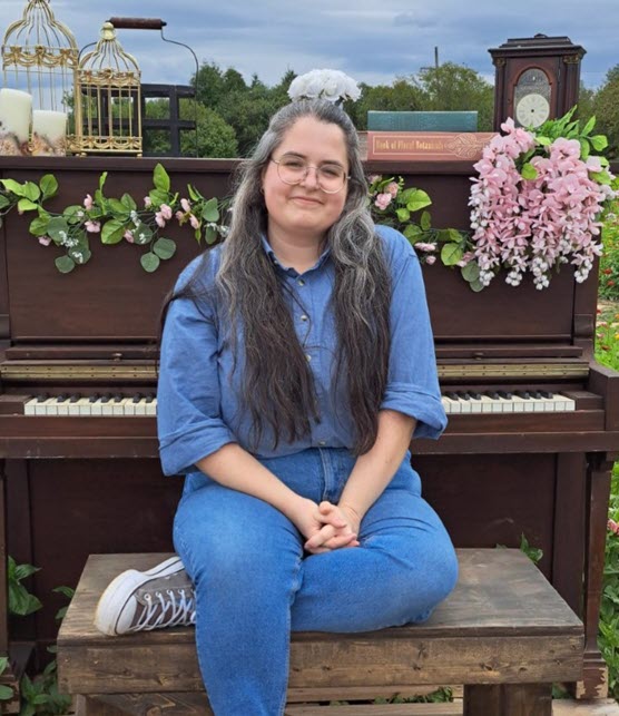 Staff member Erin sitting with her back to against a piano. 