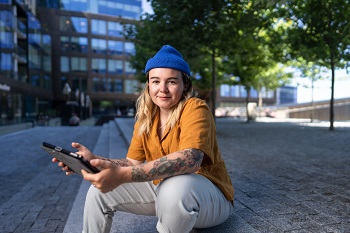 NSCC grad Anisa Francoeur sits on wooden steps along the Halifax waterfront while holding a tablet.